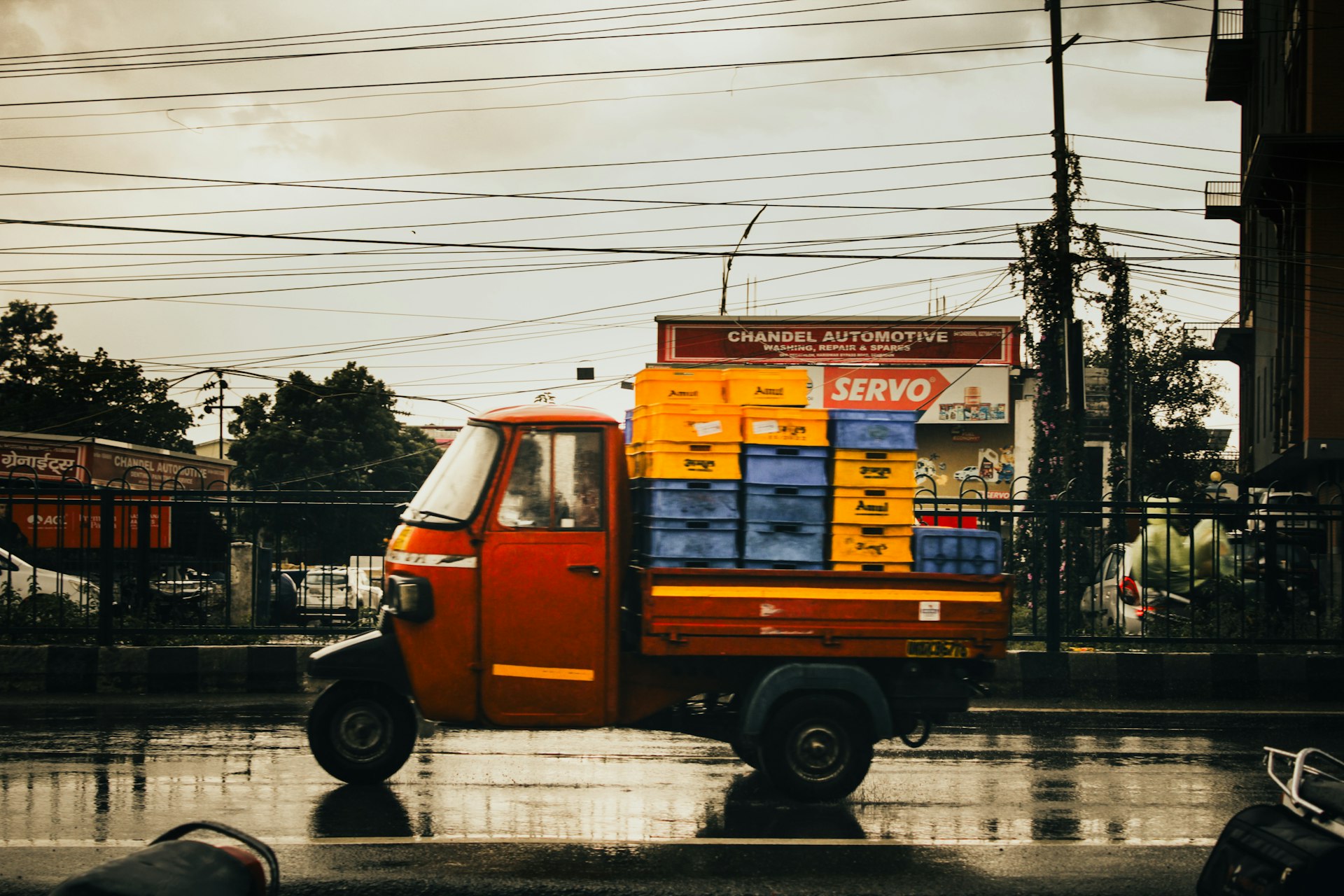 A red tuk-tuk transports crates on a wet street.